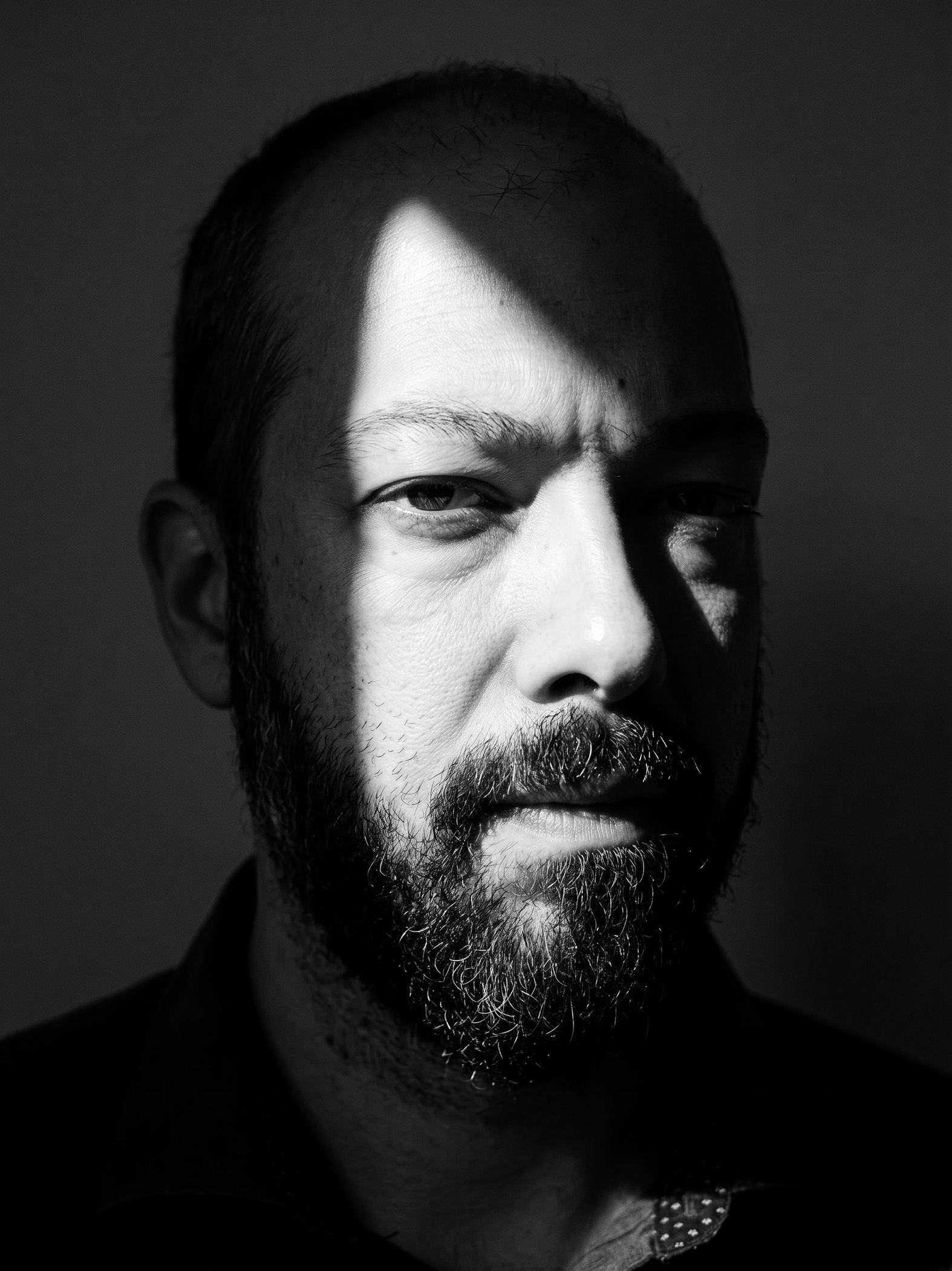 Vagelis Antoniadis, in a black-and-white portrait lit from one side against a dark background